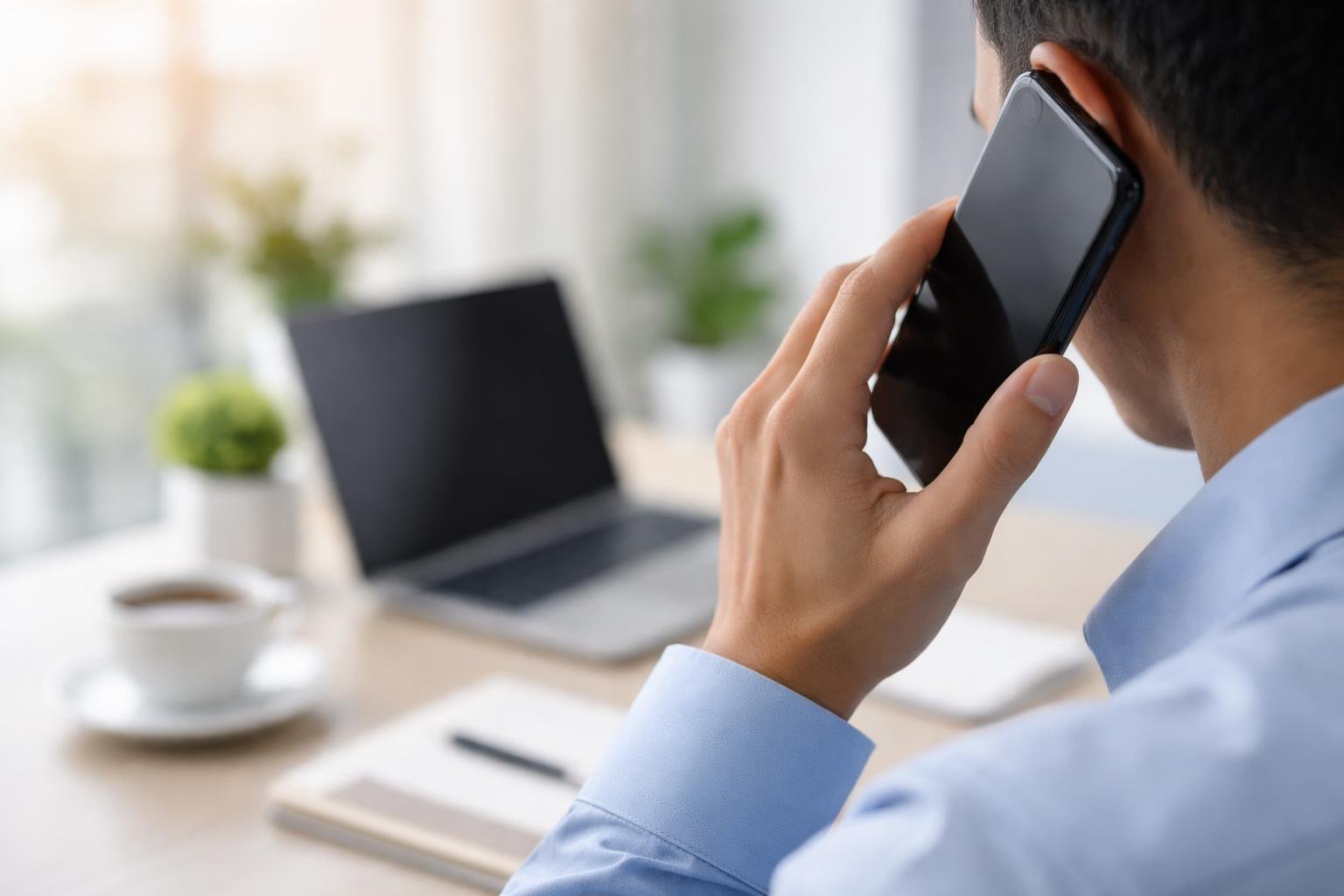 Pessoa segurando um smartphone em um escritório moderno, com laptop e planta ao fundo.