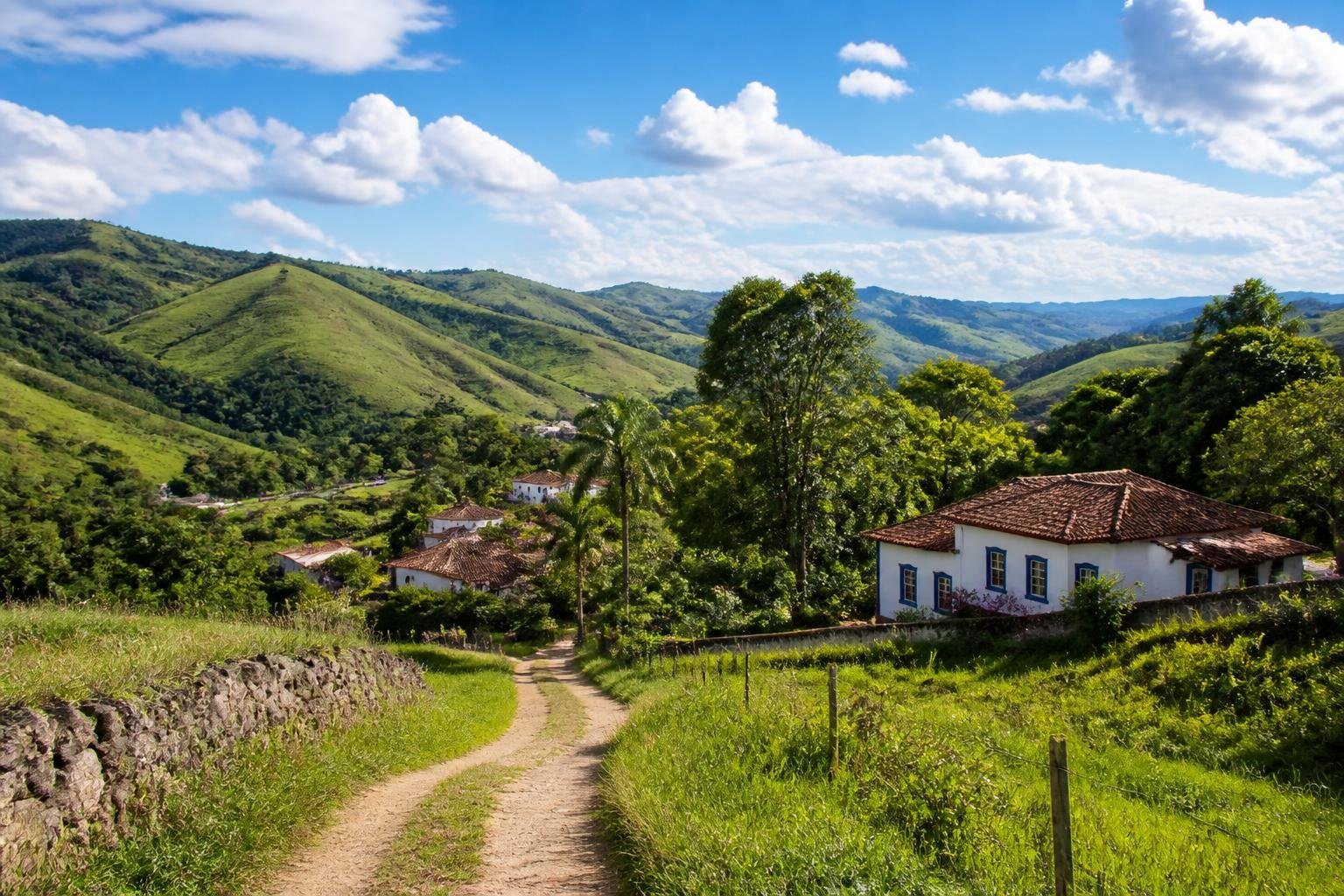 Paisagem rural de Serro, Minas Gerais, com colinas verdes, casas coloniais e céu azul com nuvens.